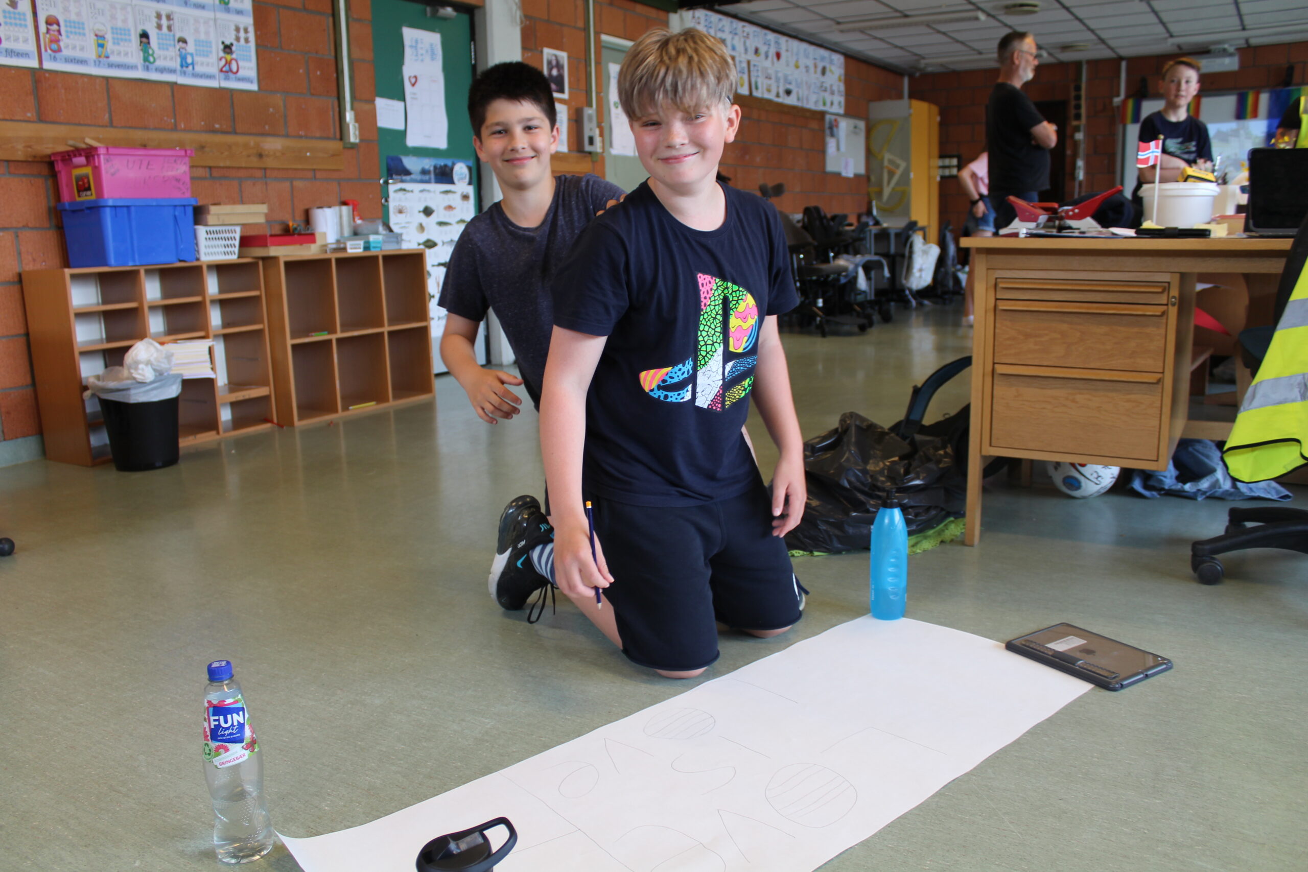 Kompisene Isak Amin Azad Myrvang (11) og Liam Niklas Legrem (12) skisser opp plakaten de skal gå med.