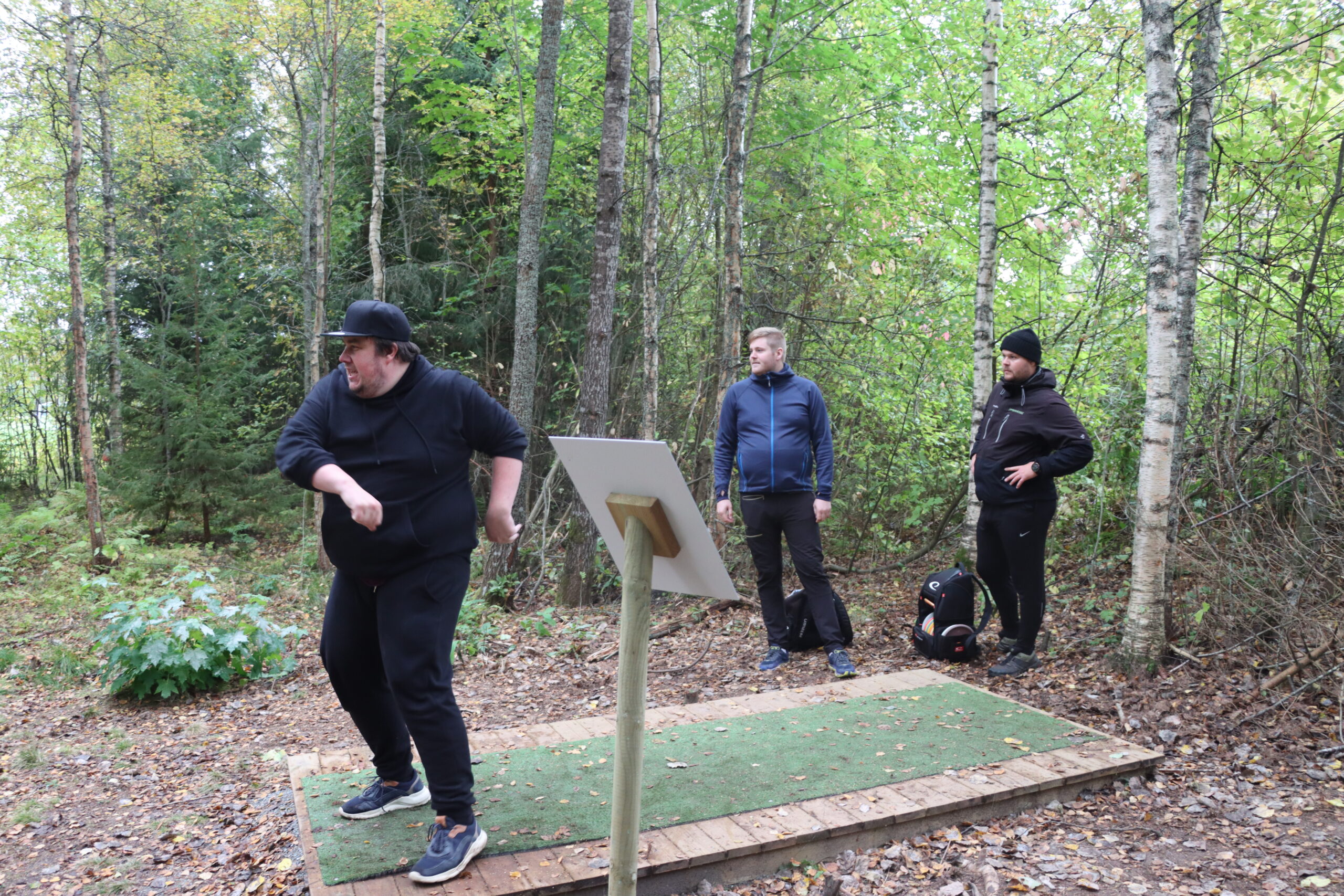 Rolf Oskar Rønhovde kaster avgårde sin frisbee i skogen. Jonas Ørbog Ødegård (t.v.) og Erlend Rønning venter på tur.