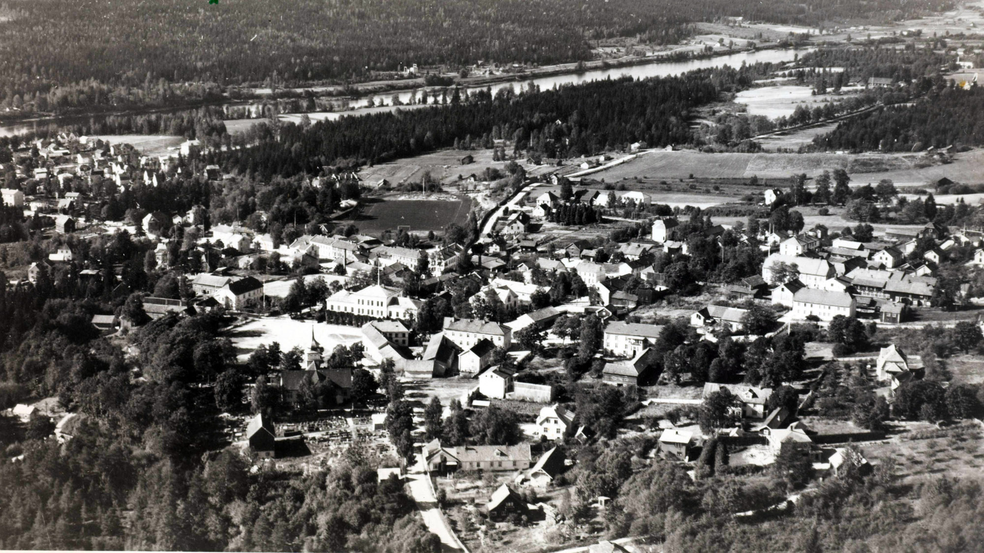 Widerøe flyfoto fra 1947 med Øvrebyen videregående skole midt i bildet. Bak sees Øvre Langelandsvei som strekker seg over åsryggen og det er en tydelig dump ned mot der Heberheimen ligger i dag. Oppe til høyre skimtes låven på Langeland Øvre.