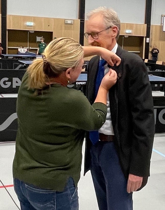 Anne Haug fra Kongsvinger og visperepsident i Norges Bordtennisforbund fester hederstegnet på Tore Eig.