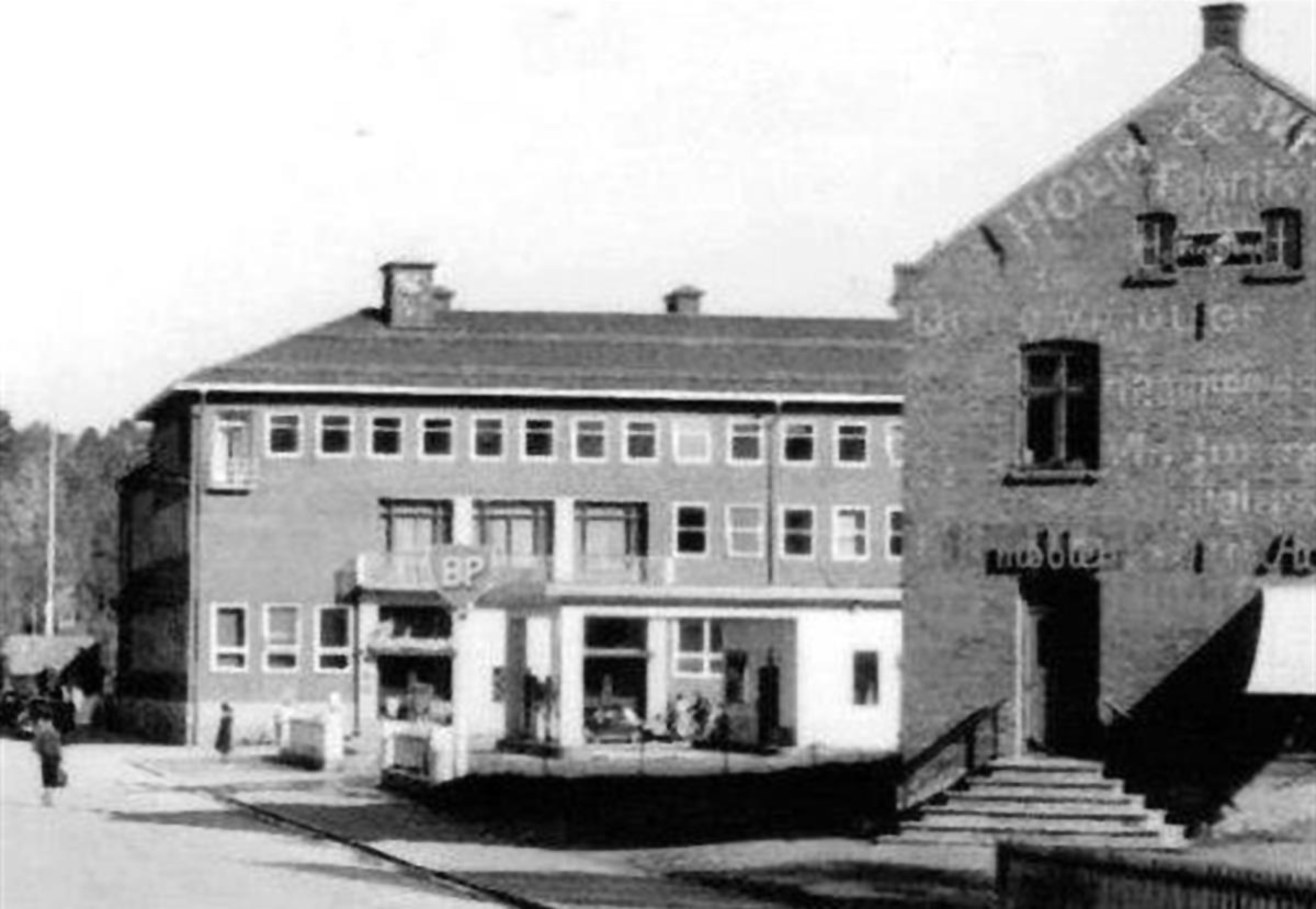 Fotografi av Storgata tatt fra enden av bybrua som viser Iversen/Hom-gården med BP-stasjonen og Rådhuset i bakgrunnen.