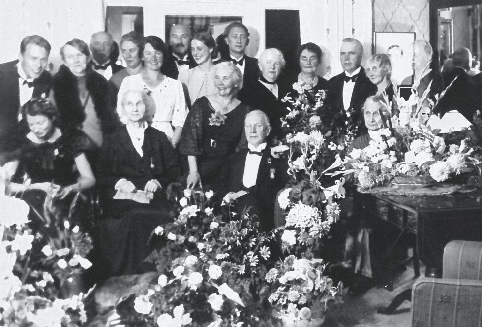 Familien Gulliksen/Schulerud, her trolig samlet ved Sigrids svoger Gunvald Gulliksen (sittende foran) sin 80-årsdag. Sigrid står bak ham til høyre, med kort mørkt hår, bak den høyeste blomsteroppsatsen.