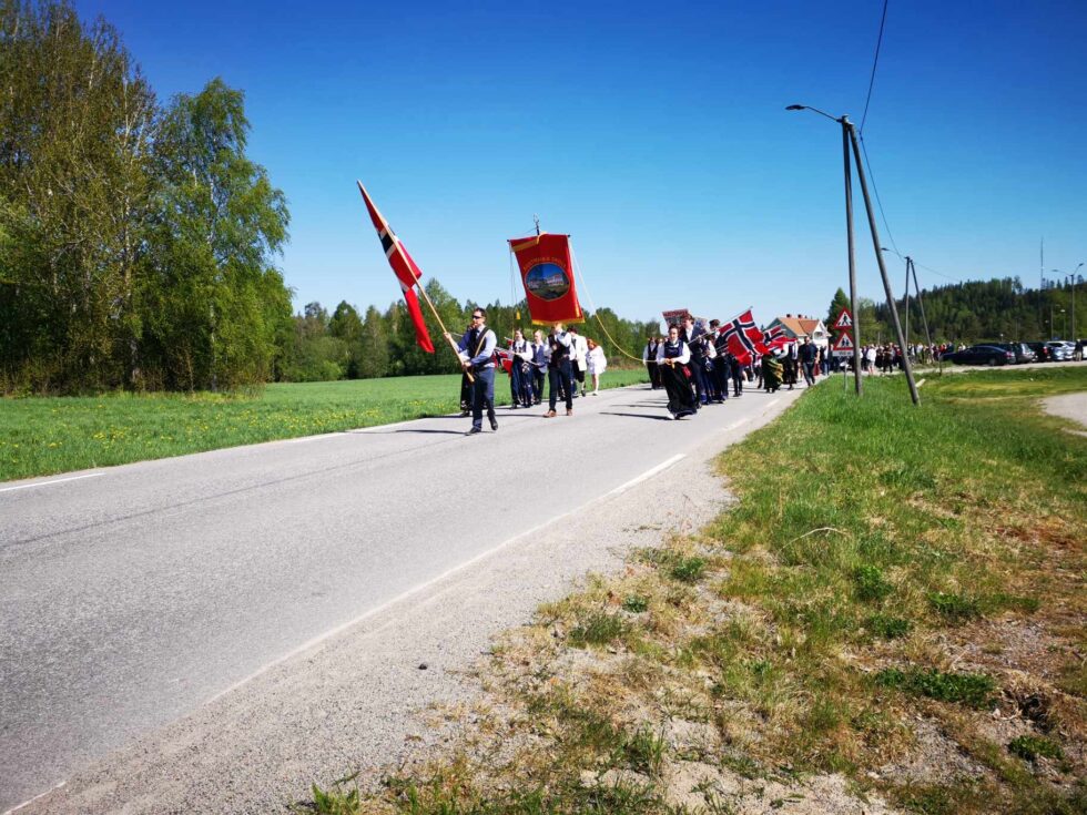 17. mai toget på Austmarka beveger seg mot kirka og skolen med "Spiken" i bakgrunnen.