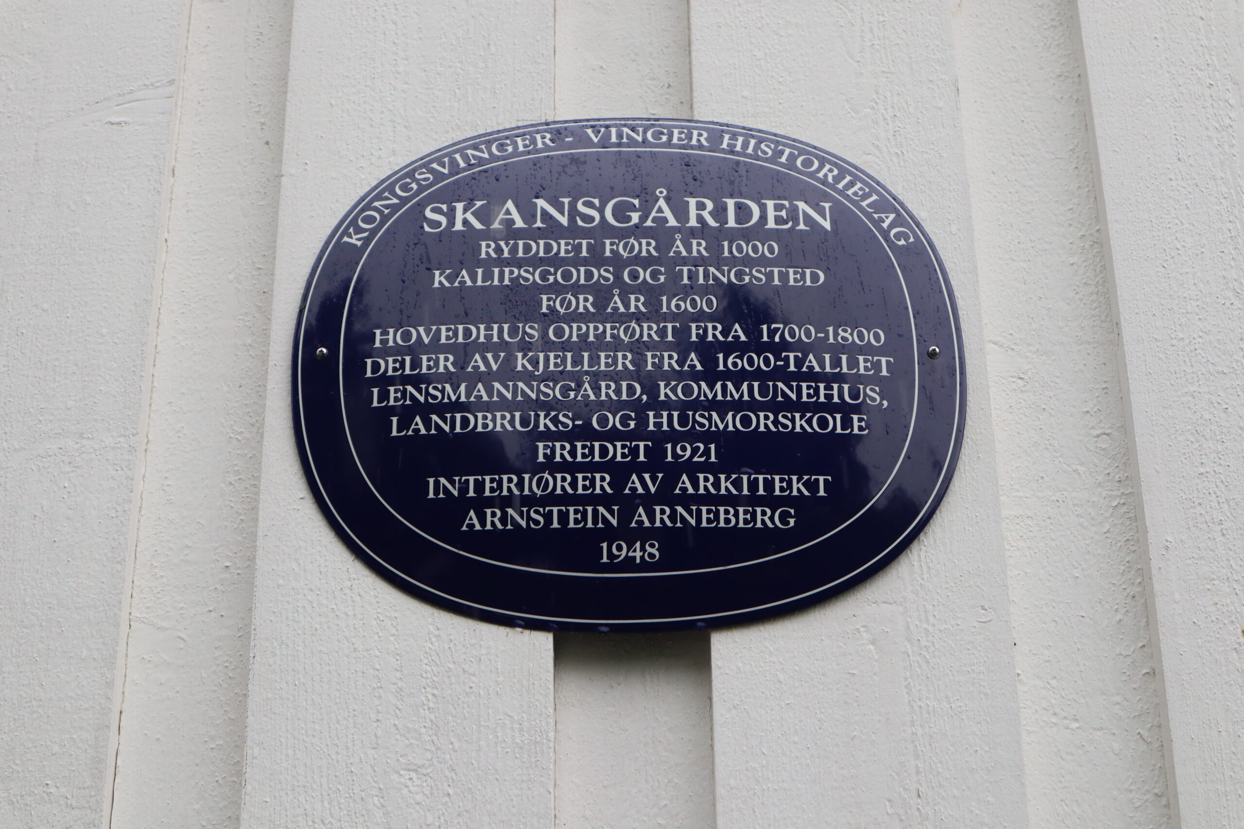 Et historisk bl&aring;tt skilt til Skansg&aring;rden: Tingsted, lensmannsg&aring;rd, kommunehus og landbruks- og husmorskole.