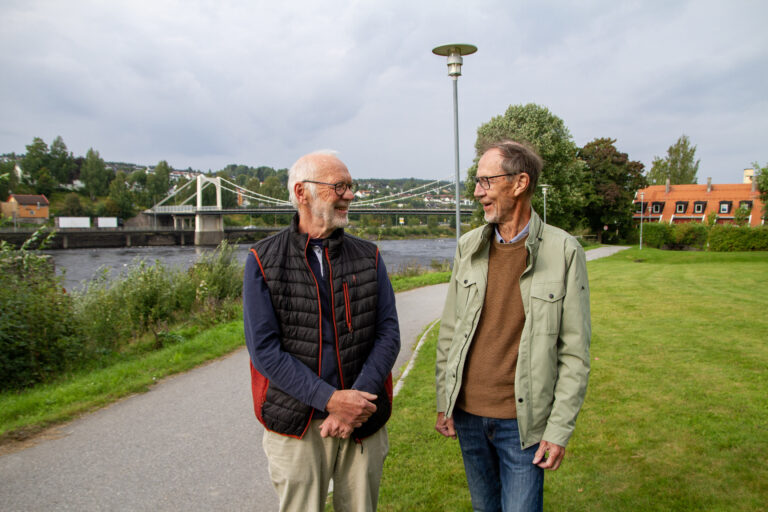 Johan-Kristian Tønder og Terje Martinsen ved strandpromenaden i Kongsvinger. Ble Nedre linje realisert ville veien gått på nordsiden av elva fra Gjemselund til Sentralskolen, og videre i en bru over til Sundehjørnet. I bakgrunnen kjører bilene på veien som ble bygget i 1991, dagens E16.
