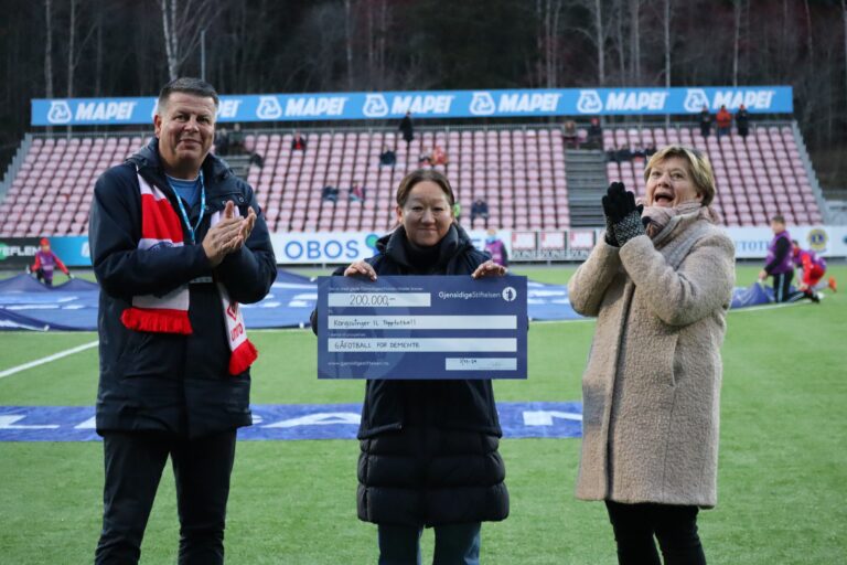 Markedsansvarlig i KIL Toppfotball, Rune Lundgren (t.v.) og Marianne Aspebakken i Kongsvinger Demensforening (midten) er overveldet over støtten som Jannicke S. Mykkestue (t.h.) kunne overrekke på vegne av Gjensidigestiftelsen rett før lørdagens hjemmekamp på Gjemselund.