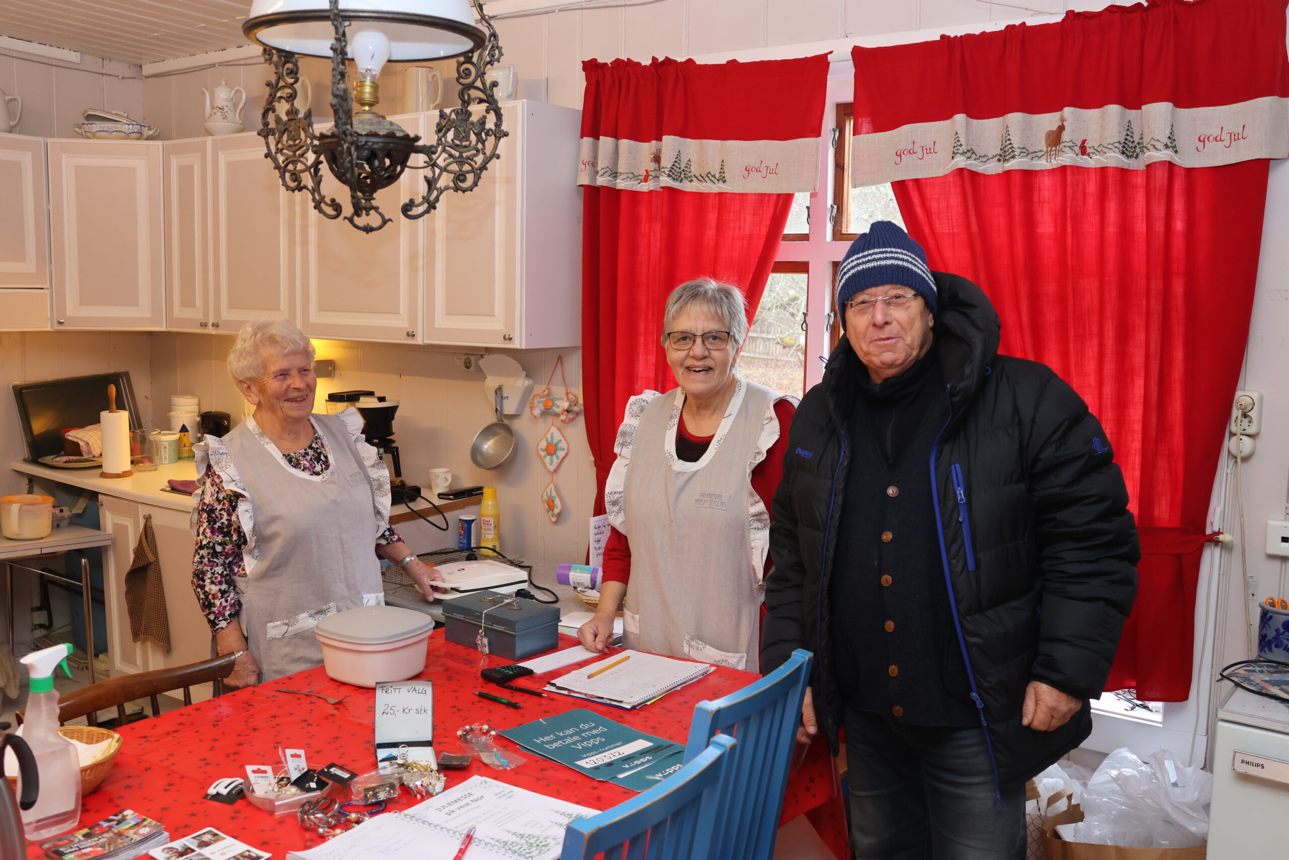 Åshild Nymoen (t.v.) har ansvaret for vafler og kaffe, mens Eva Helen Nygård bistår kunden Finn Hansen slik at han får betalt for topplua han har kjøt på julemessa.