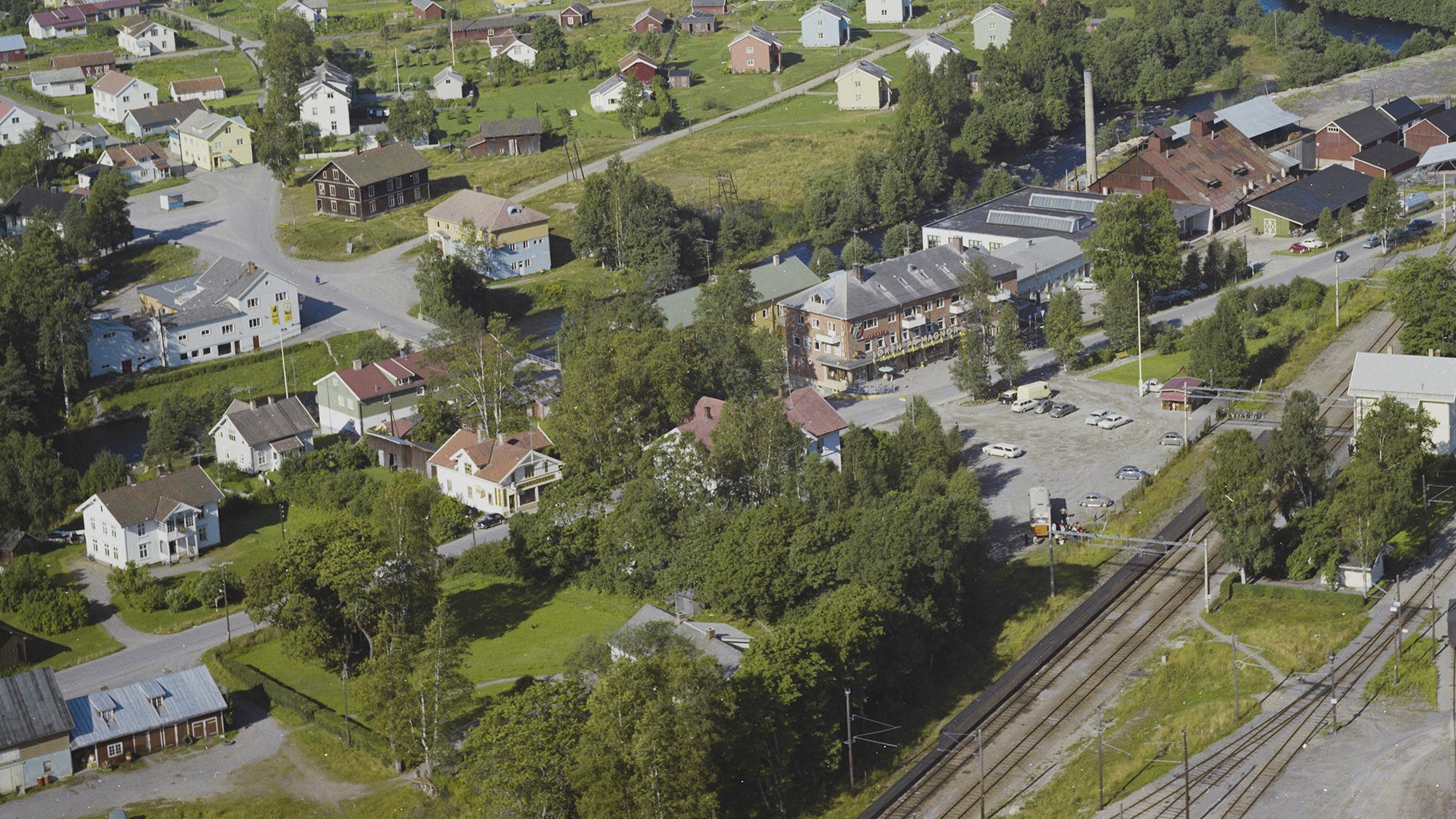 Flyfoto av Magnor fra 1965 med glassverket oppe til høyre. Huset nederst i bildet med grått tak er Rasta, og ved siden av ligger den ganle tollgården.