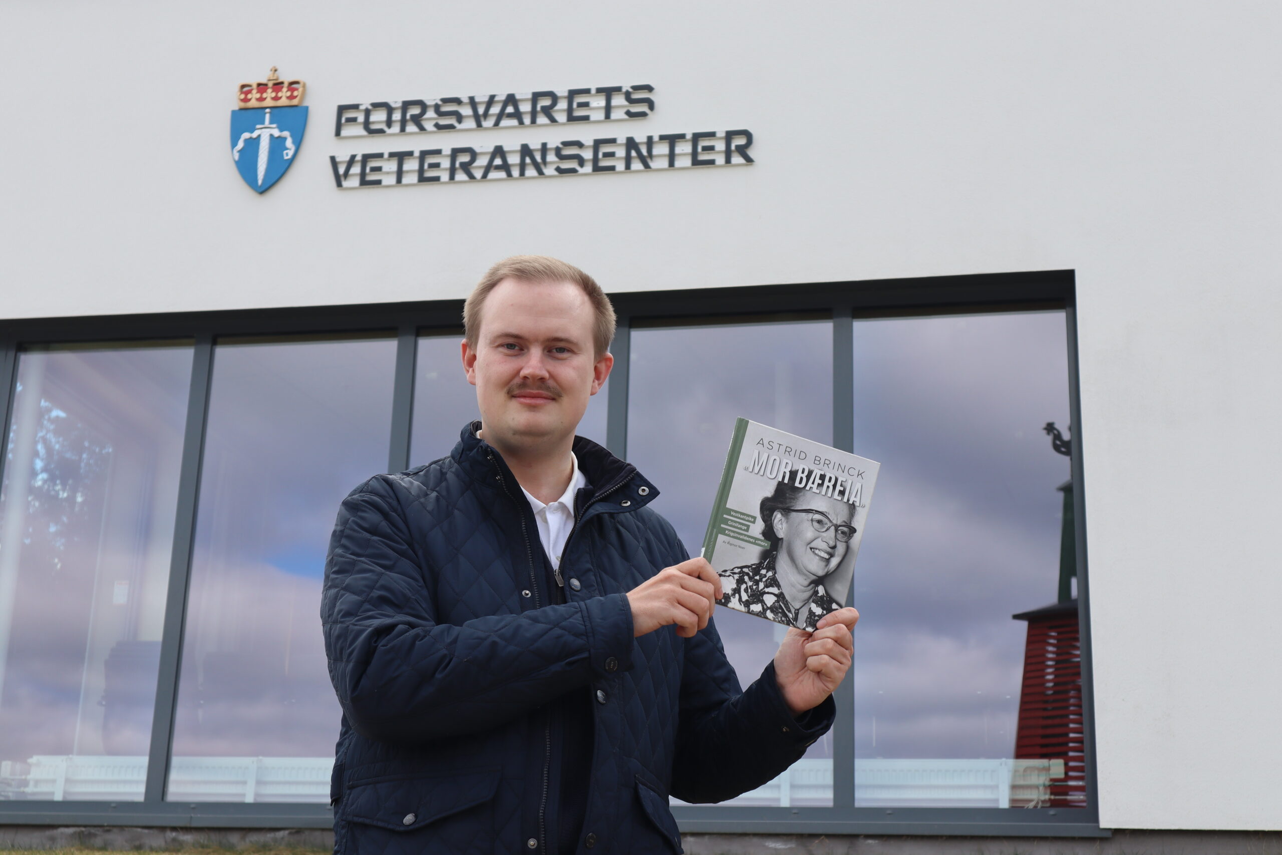 Oskar Aanmoen fra Kongsvinger-Vinger Historielag gleder seg over å kunne hedre Mor Bæreia, Astrid Brinck på 80 årsjubileet for frigjøringsdagen. Her foran Veteransenteret med boka Astrid Brinck: Mor Bæreia, skrevet av Rigmor Noer.