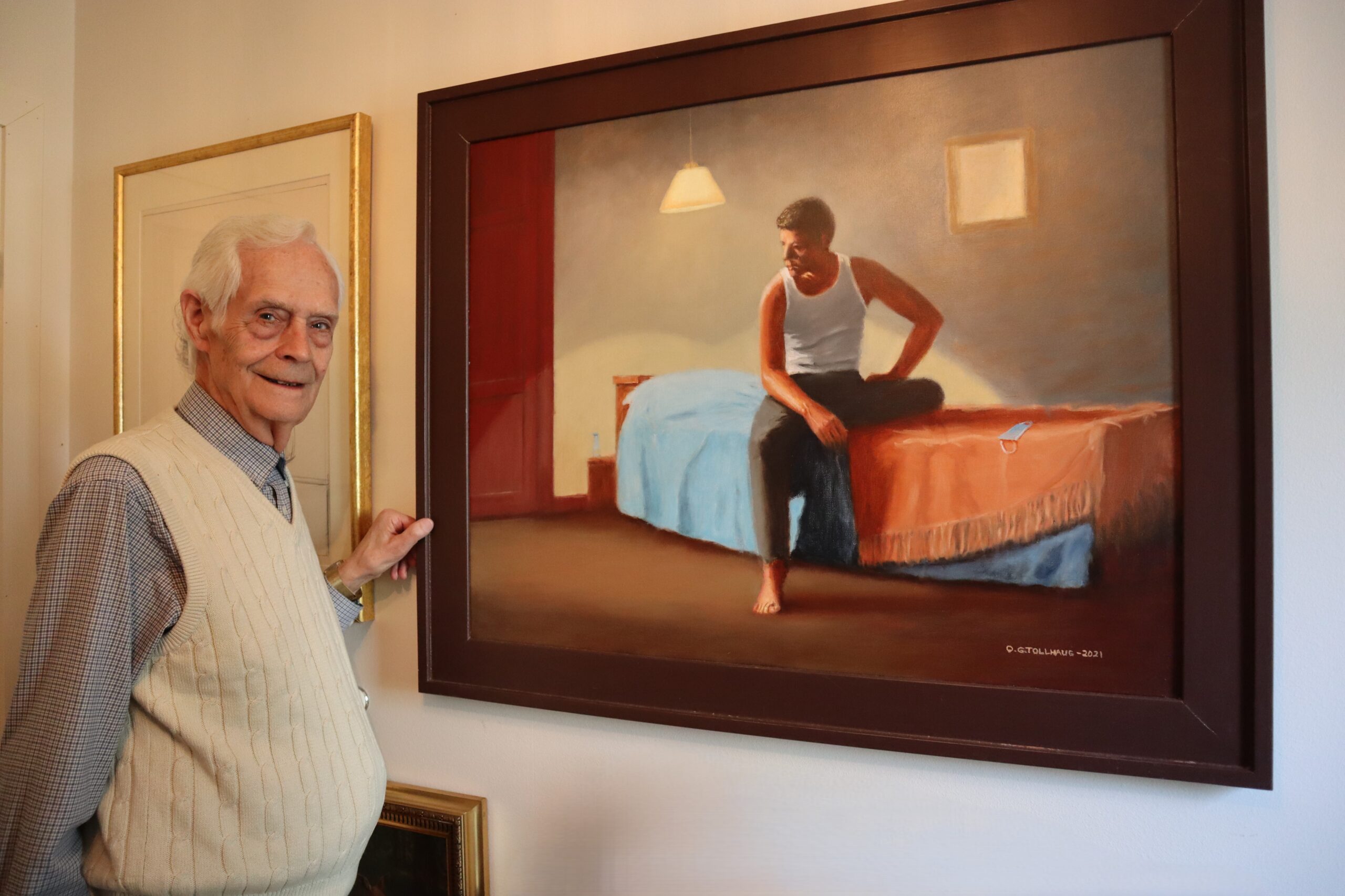 Her står Asbjørn foran et av mange kunstverk han har, laget av Ole Gunnar Tollhaug. Bildet er malt i 2021, og symboliserer ensomheten under covid-pandemien, med et munnbind liggende på sengen.