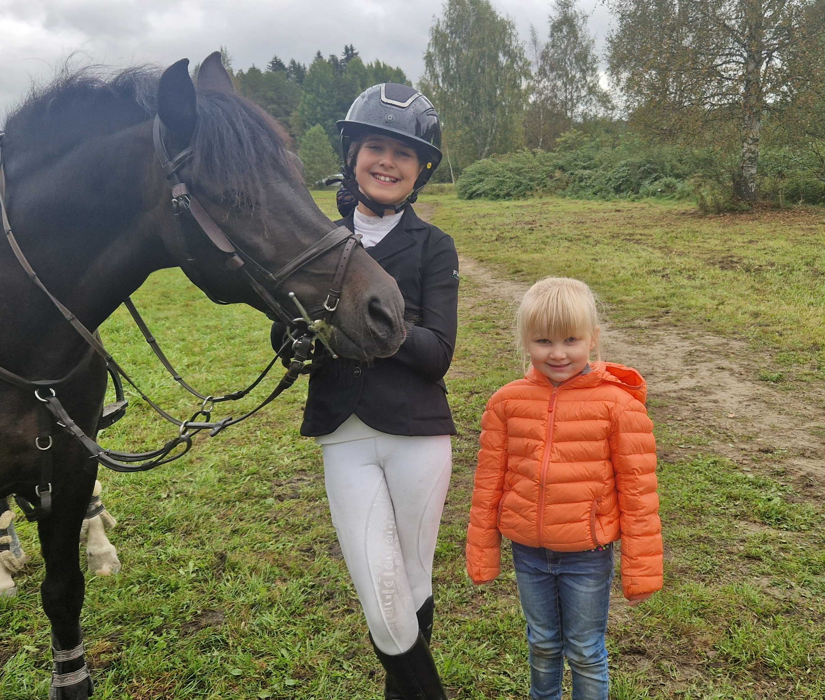 Tindra Rønningen (11) og Tiril Rønningen (5) med hesten Todd. Tindra forteller at stevner er det som motiverer hun, og at det er moro å hoppe med hesten.
