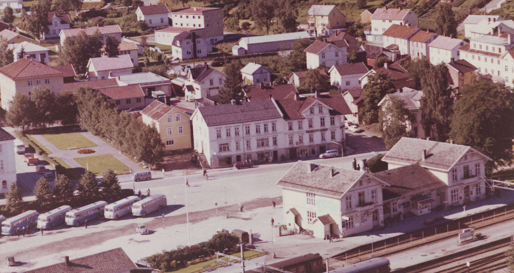 Widerøe Flyveselskaps flyfoto fra 1961 som viser jernbanestasjonen og Victoria Hotell på den andre siden av Glommengata. Grand Hotell skimtes oppe til høyre.