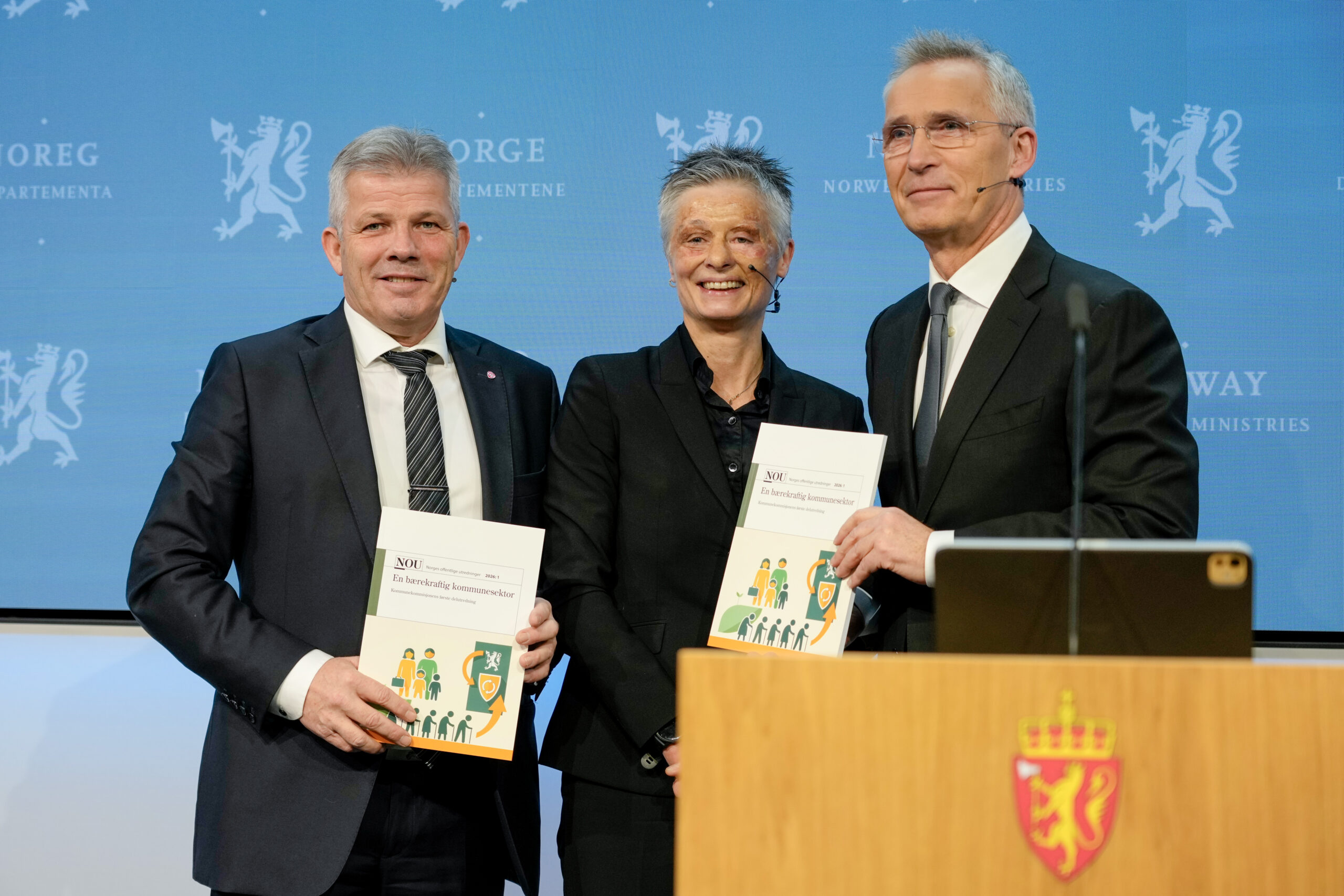 Signy Irene Vabo overrekker kommunekommisjonens første rapport til kommunal- og distriktsminister Bjørnar Skjæran og finansminister Jens Stoltenberg. Her foreslås det blant annet å fjerne lærernormen